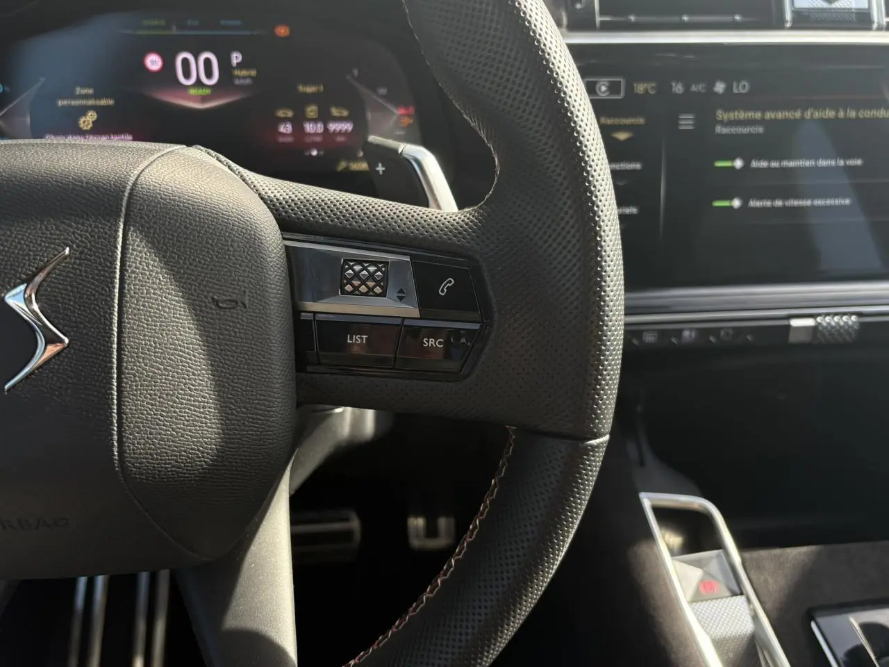 Gros plan sur le volant en cuir perforé noir avec surpiqûres Carmin et Or du DS7 2024, tableau de bord numérique en arrière-plan.