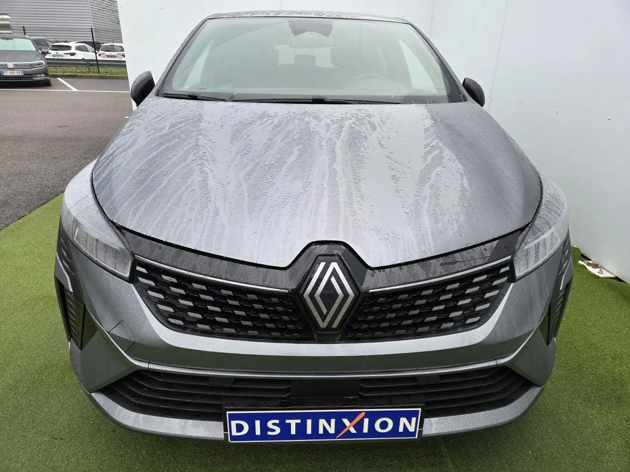 Vue avant d'une Renault Clio V gris schiste métal avec calandre noire et logo Renault central sous la pluie.