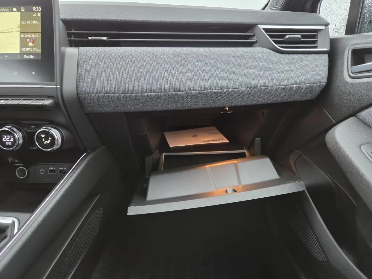 Intérieur de la Renault Clio 2025, vue de la boîte à gants ouverte avec tableau de bord gris mélangé et écran tactile visible.