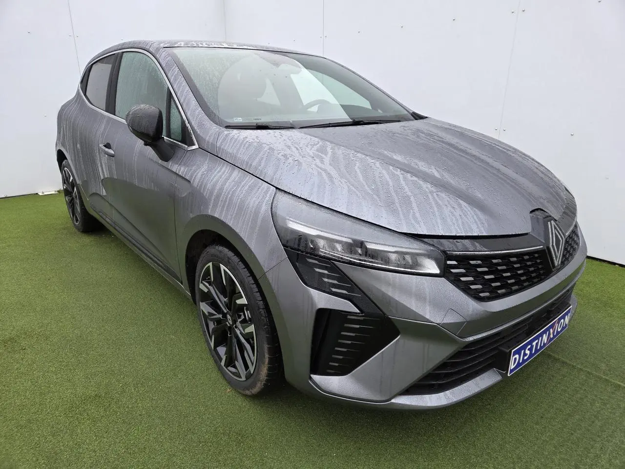 Vue 3/4 avant gauche d'une Renault Clio 2025 gris schiste métal avec jantes alliage noires et contours chromés.