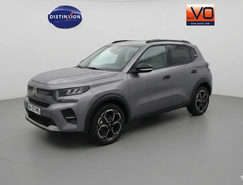 Vue 3/4 avant droit d'une Citroën C3 gris métallisé 2025 avec jantes alliage 17 pouces et barres de toit noires.