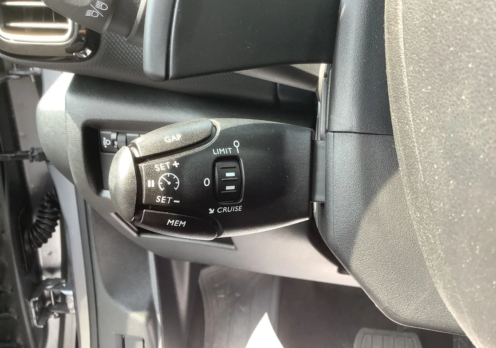Gros plan sur la commande de régulateur de vitesse noire dans l’habitacle gris foncé du Citroën C5 Aircross Hybrid 2024.