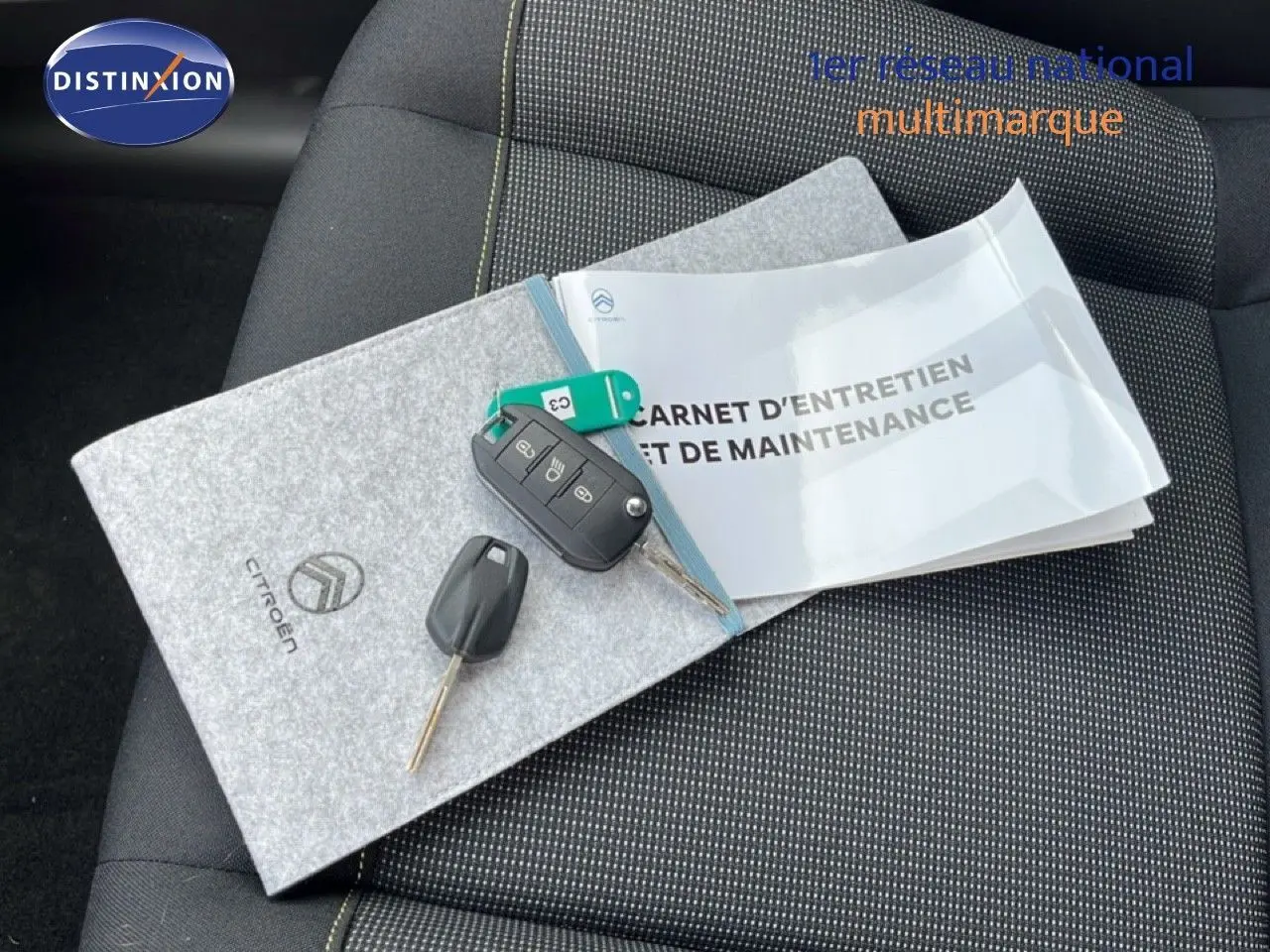 Vue rapprochée du carnet d’entretien Citroën et des clés posés sur un siège tissu gris noir de Citroën C3 2024.