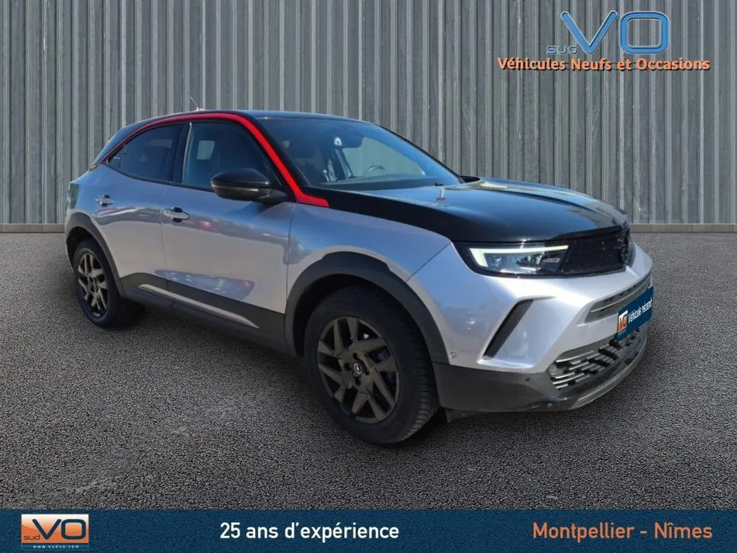 Opel Mokka gris clair vue 3/4 avant droit avec capot noir et jantes alliage 18 pouces sur fond neutre.