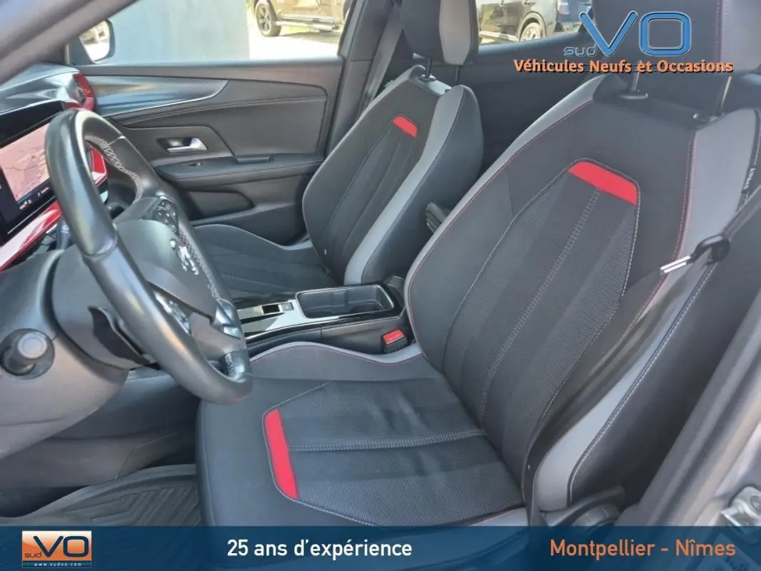 Vue intérieure côté conducteur de l'Opel Mokka gris clair 2022, sièges noirs avec surpiqûres rouges et volant cuir.