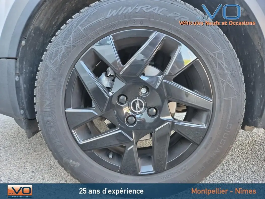 Gros plan sur la jante alliage noire 18 pouces avec logo Opel du côté gauche d’un Opel Mokka gris clair 2022.