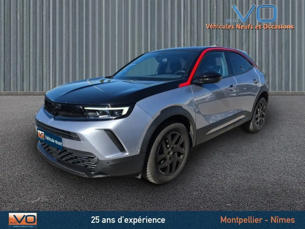 Opel Mokka gris clair 3/4 avant droit avec toit noir et montant rouge, jantes alliage noires, vitres surteintées.