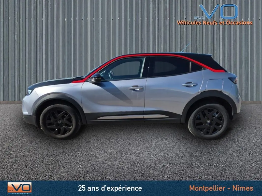 Profil droit d'un Opel Mokka gris clair 2022 avec toit noir et bande rouge, jantes alliage noires de 18 pouces.