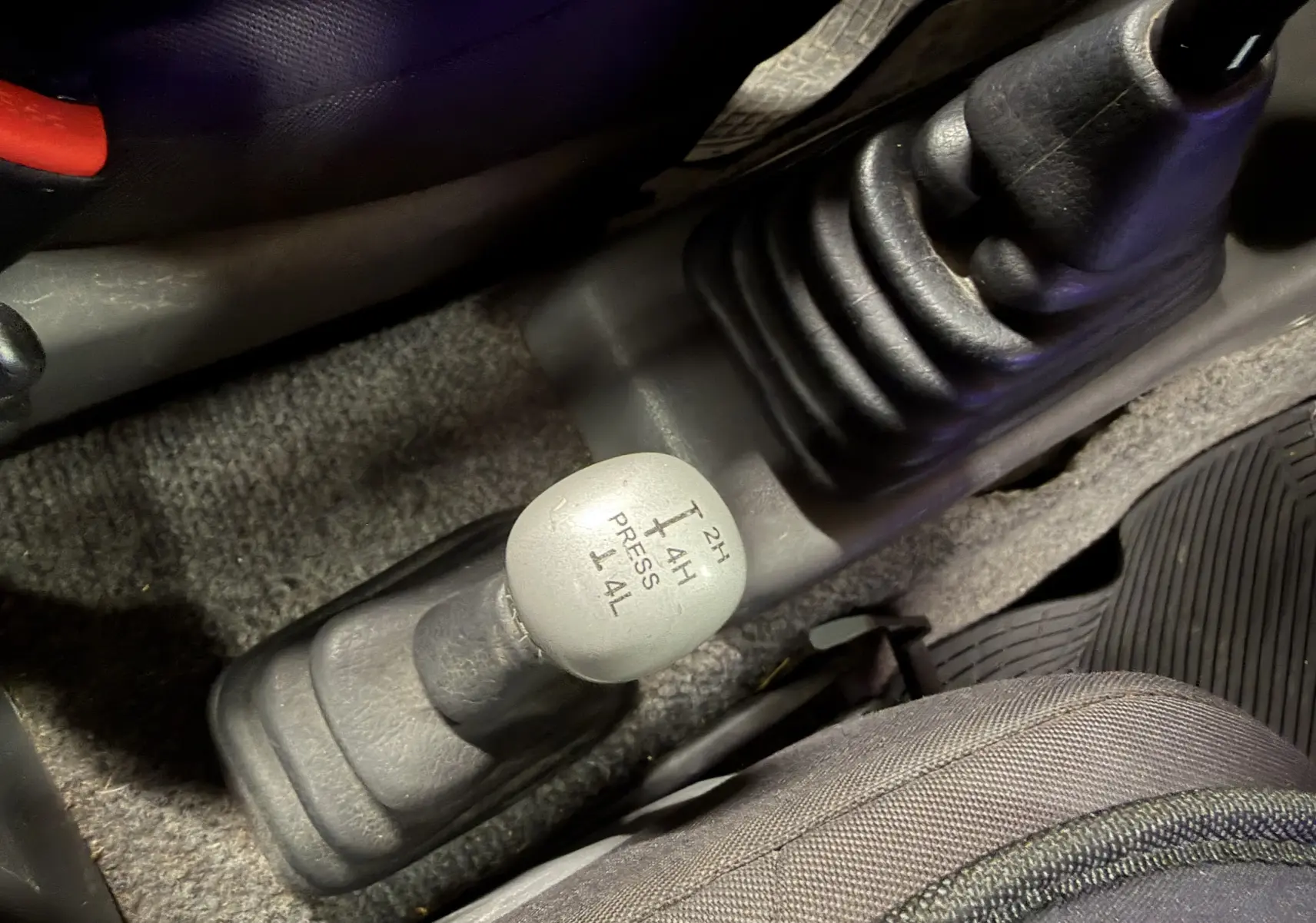 Gros plan sur la commande de boîte de transfert manuelle du Suzuki Jimny Cabriolet gris, intérieur côté conducteur.