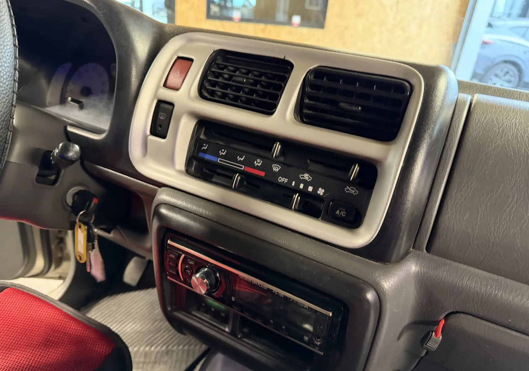 Vue rapprochée de la console centrale grise du Suzuki Jimny Cabriolet 2005, avec radio et commandes de climatisation.