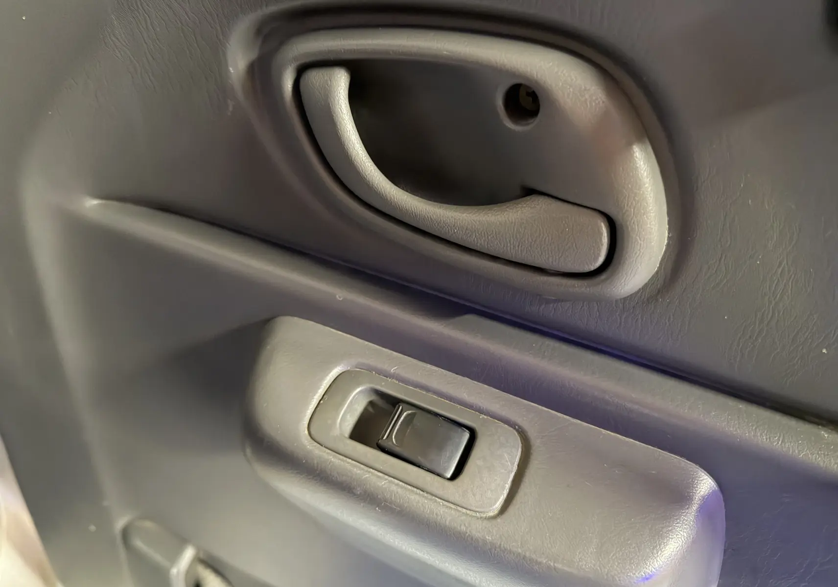 Gros plan sur la poignée de porte intérieure grise avec commande de vitre électrique du Suzuki Jimny Cabriolet 2005.