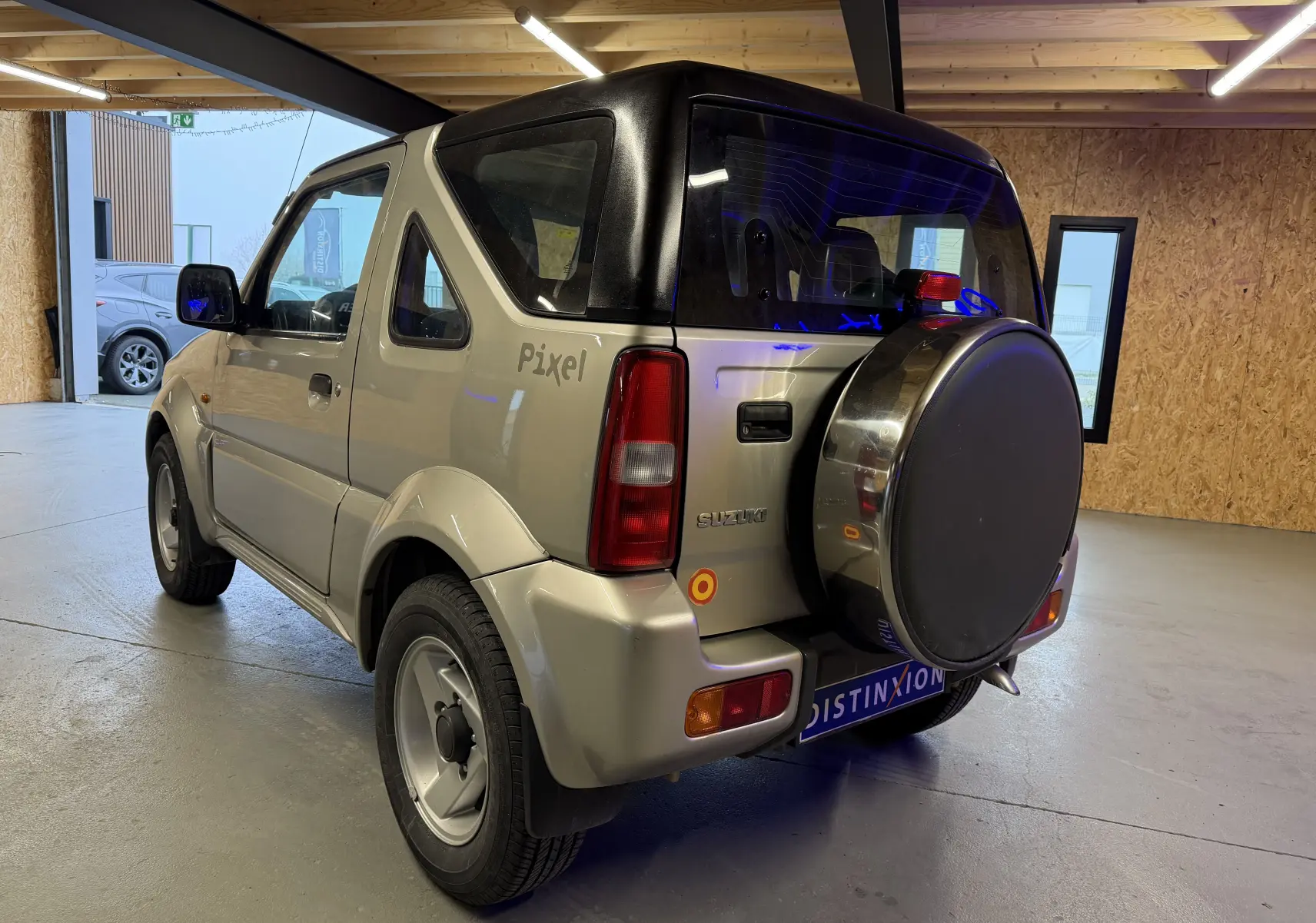 Vue 3/4 arrière droite d'un Suzuki Jimny Cabriolet gris 2005 avec hard-top, roue de secours et jantes alu.