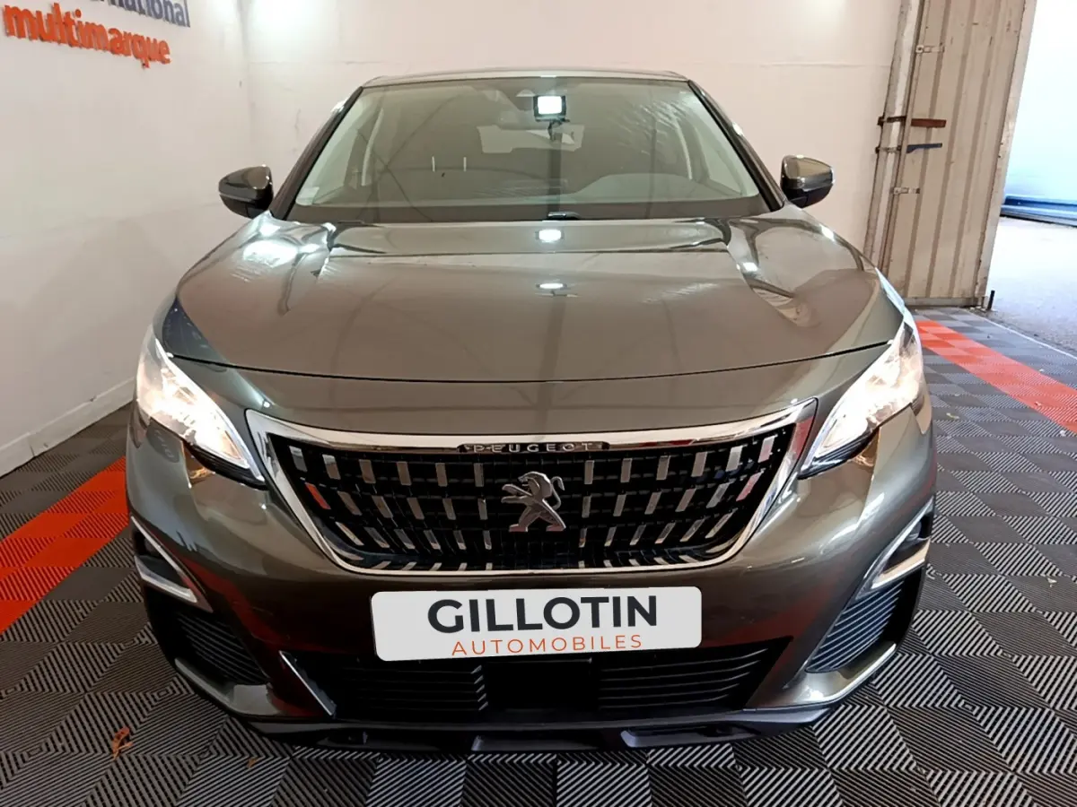 Peugeot 3008 gris foncé vue de face, mettant en valeur la calandre distinctive et les phares allumés.