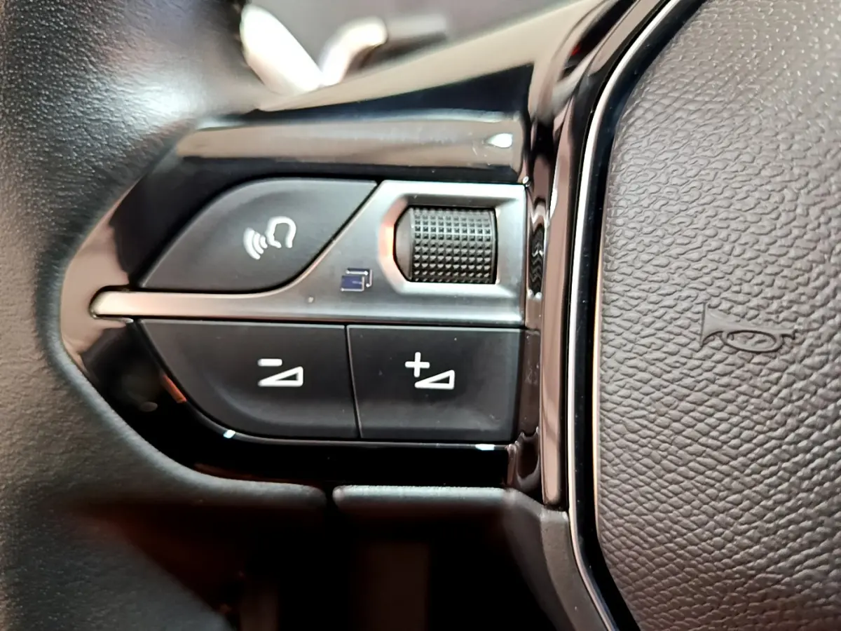 Gros plan sur les commandes gauche du volant cuir noir du Peugeot 3008 gris foncé, avec boutons de volume et téléphone.