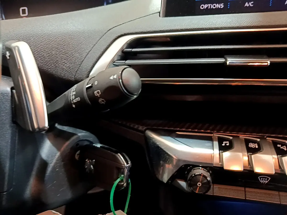 Détail du tableau de bord et commandes argentées du Peugeot 3008 gris foncé, avec clé insérée et touches fonctionnelles visibles.