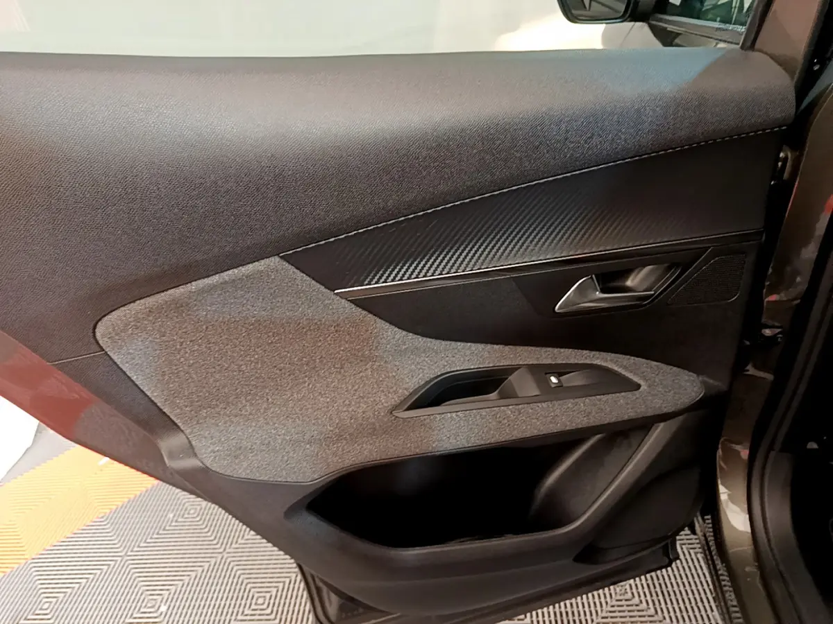 Gros plan sur la garniture intérieure de la porte avant droite du Peugeot 3008 gris foncé, avec insert effet carbone.