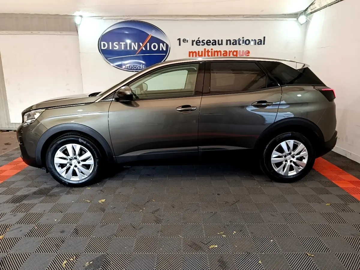 Profil côté gauche d'un Peugeot 3008 gris foncé 2020 dans un showroom avec sol en damier noir et rouge.