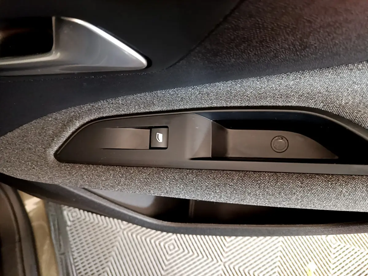 Gros plan sur la commande de lève-vitre côté conducteur, tissu gris foncé et poignée intérieure argentée du Peugeot 3008 2020.