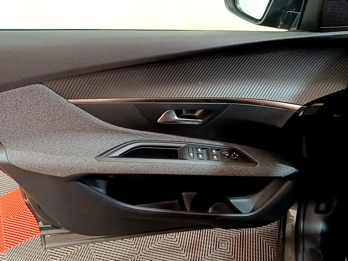 Intérieur côté gauche de la porte d'une Peugeot 3008 gris foncé, avec commandes électriques et finition carbone.