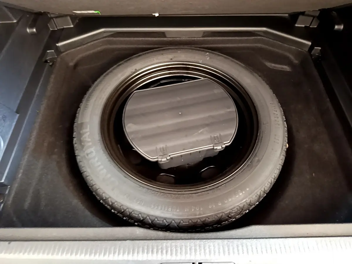 Roue de secours dans le coffre du Peugeot 3008 gris foncé, vue plongeante centrée sur le pneu de secours.