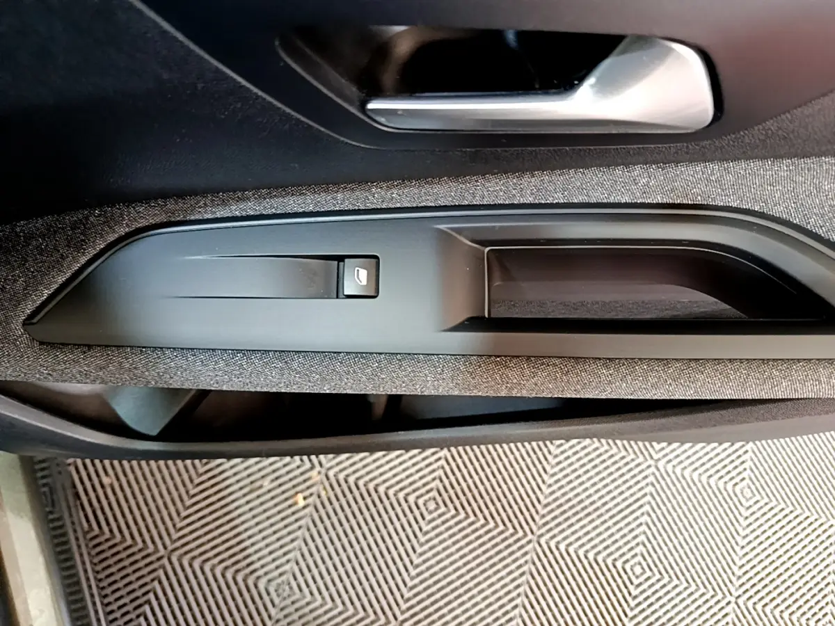 Poignée intérieure côté conducteur du Peugeot 3008 gris foncé, avec bouton de verrouillage des portes intégré.