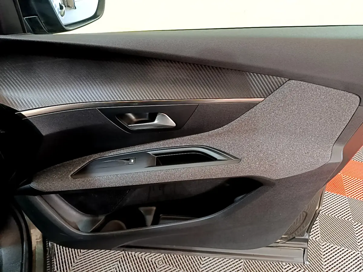 Gros plan sur la porte côté conducteur du Peugeot 3008 gris foncé, avec insert imitation carbone et commande de vitre.