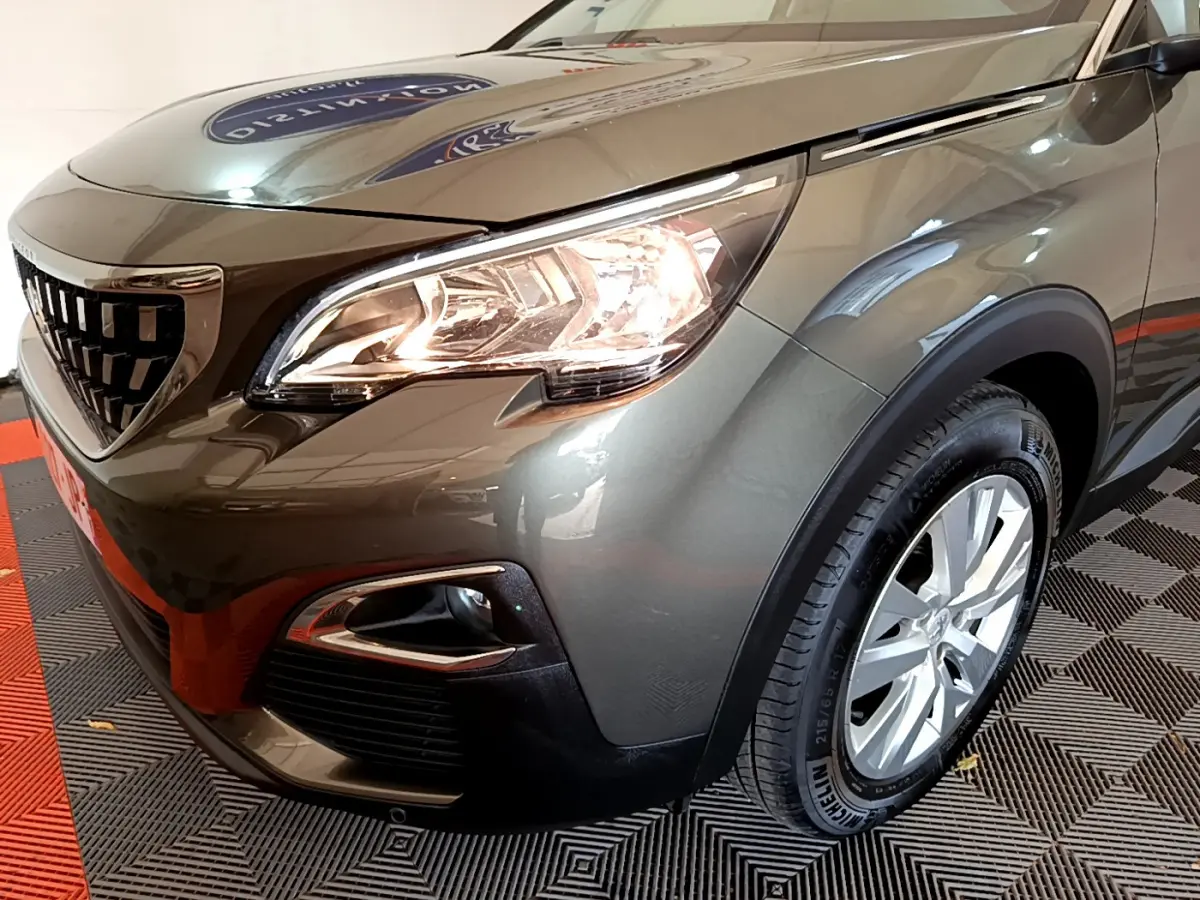 Vue 3/4 avant droit d'un Peugeot 3008 gris foncé avec phares allumés et jantes alliage visibles.