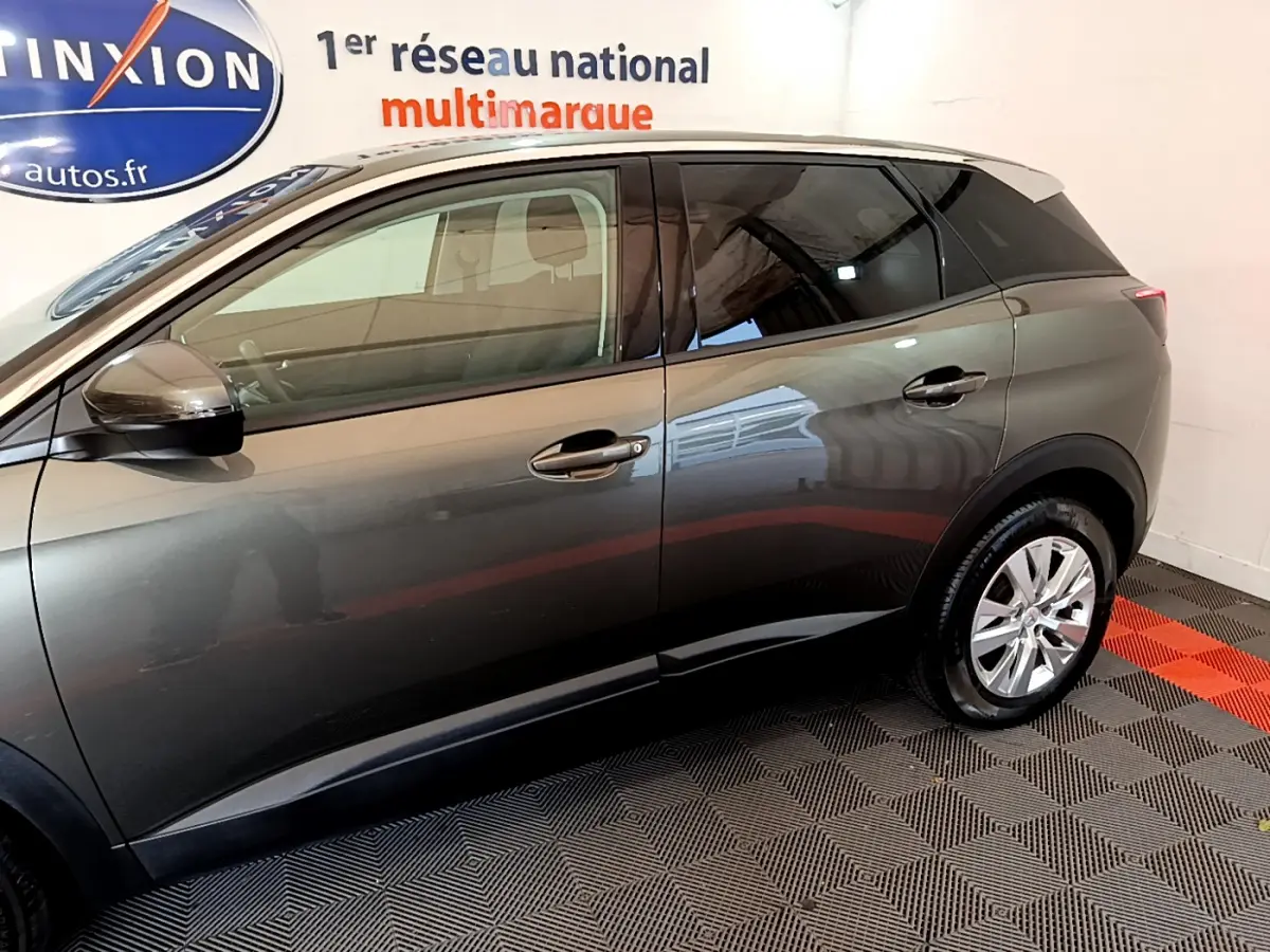 Profil côté gauche du Peugeot 3008 gris foncé 2020 dans un showroom avec sol à damier noir et rouge.