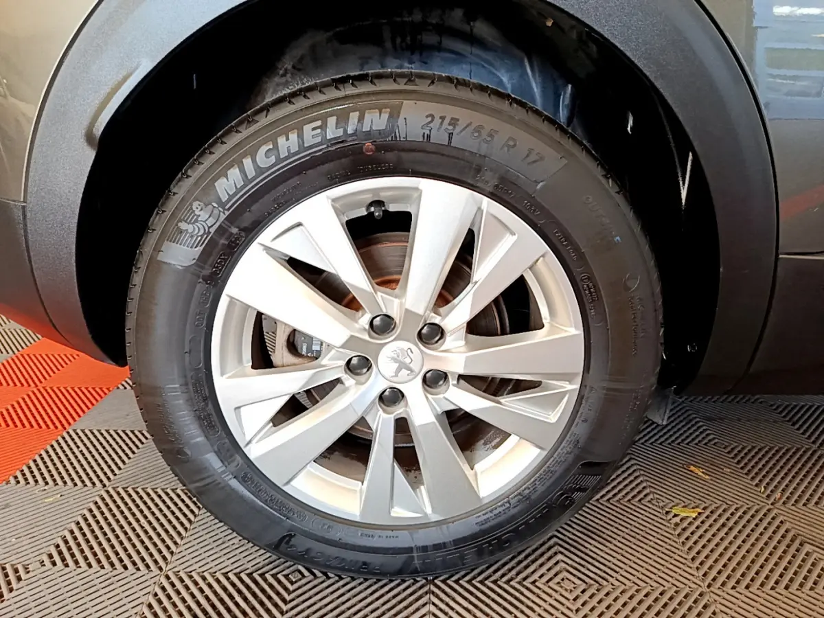 Gros plan sur la roue avant droite d’un Peugeot 3008 gris foncé, mettant en valeur la jante alliage et le pneu Michelin.
