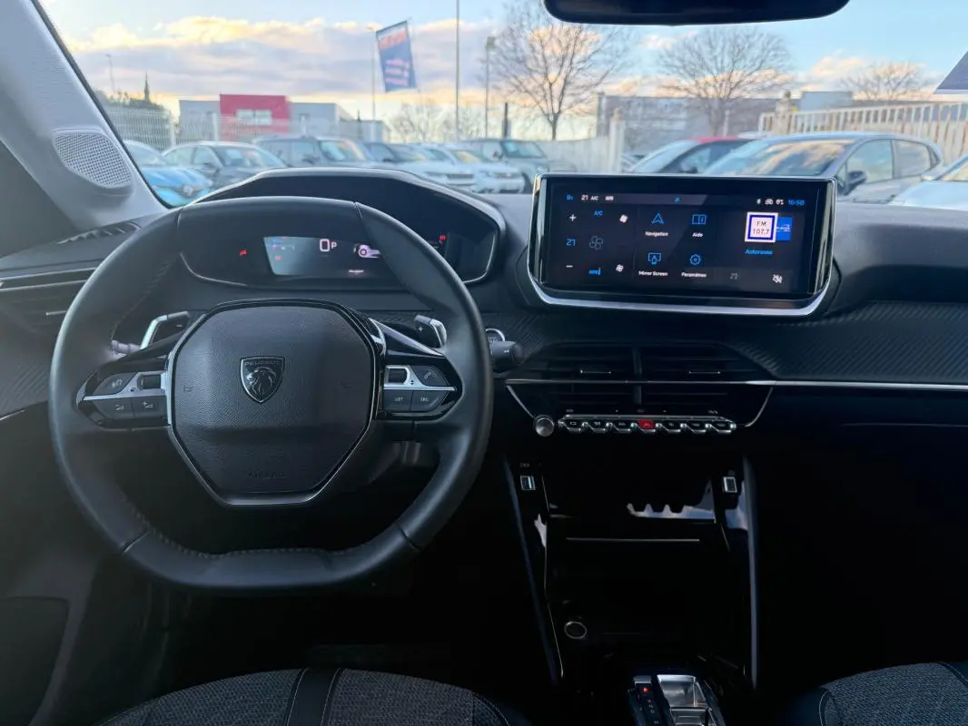 Vue intérieure frontale du poste de conduite noir de la Peugeot 208 Hybrid 110 e-DCS6 Allure avec écran tactile et volant multifonction.