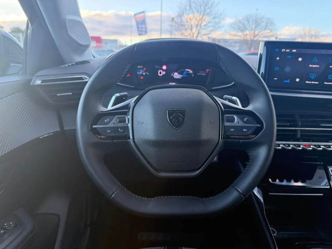 Vue intérieure centrée sur le volant cuir noir de la Peugeot 208 Hybrid 110, avec tableau de bord numérique et écran tactile.