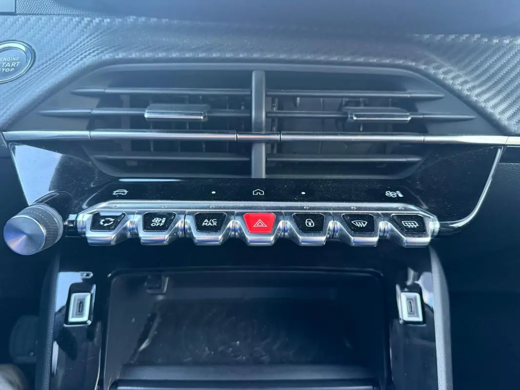 Gros plan sur la console centrale noire du Peugeot 208 Hybrid 110, montrant les boutons de commande et la grille d’aération.