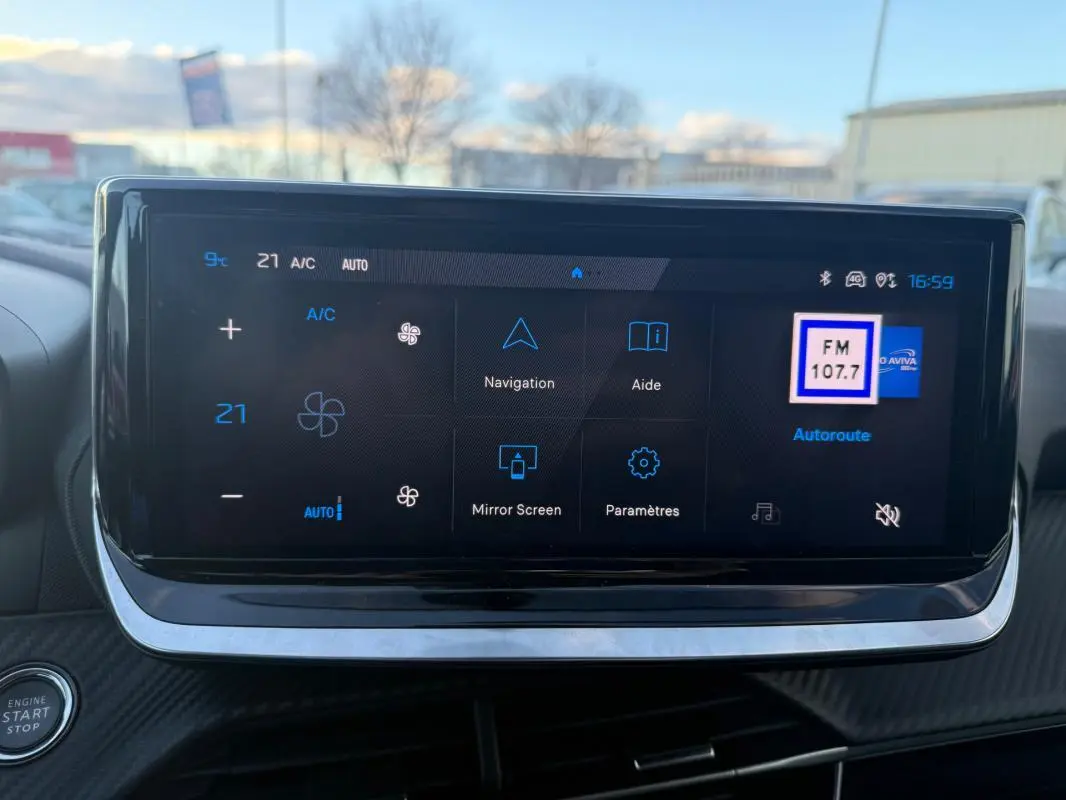 Écran tactile du tableau de bord de la Peugeot 208 Hybrid 110 noir, affichant la climatisation et la radio FM.