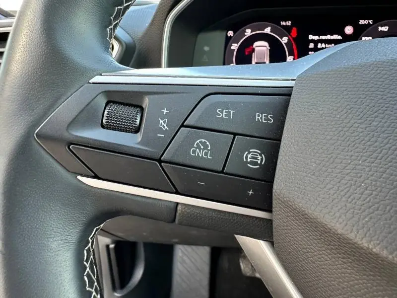 Gros plan sur les commandes du volant à gauche du SEAT LEON ST gris magnétique, avec affichage numérique en arrière-plan.