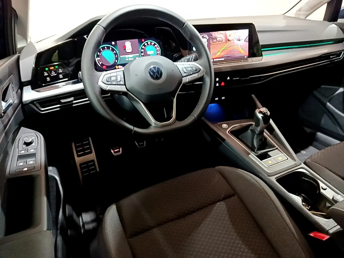 Intérieur avant d'une Volkswagen Golf 2022, vue du conducteur, volant cuir, écran tactile et levier de vitesse manuel visibles.