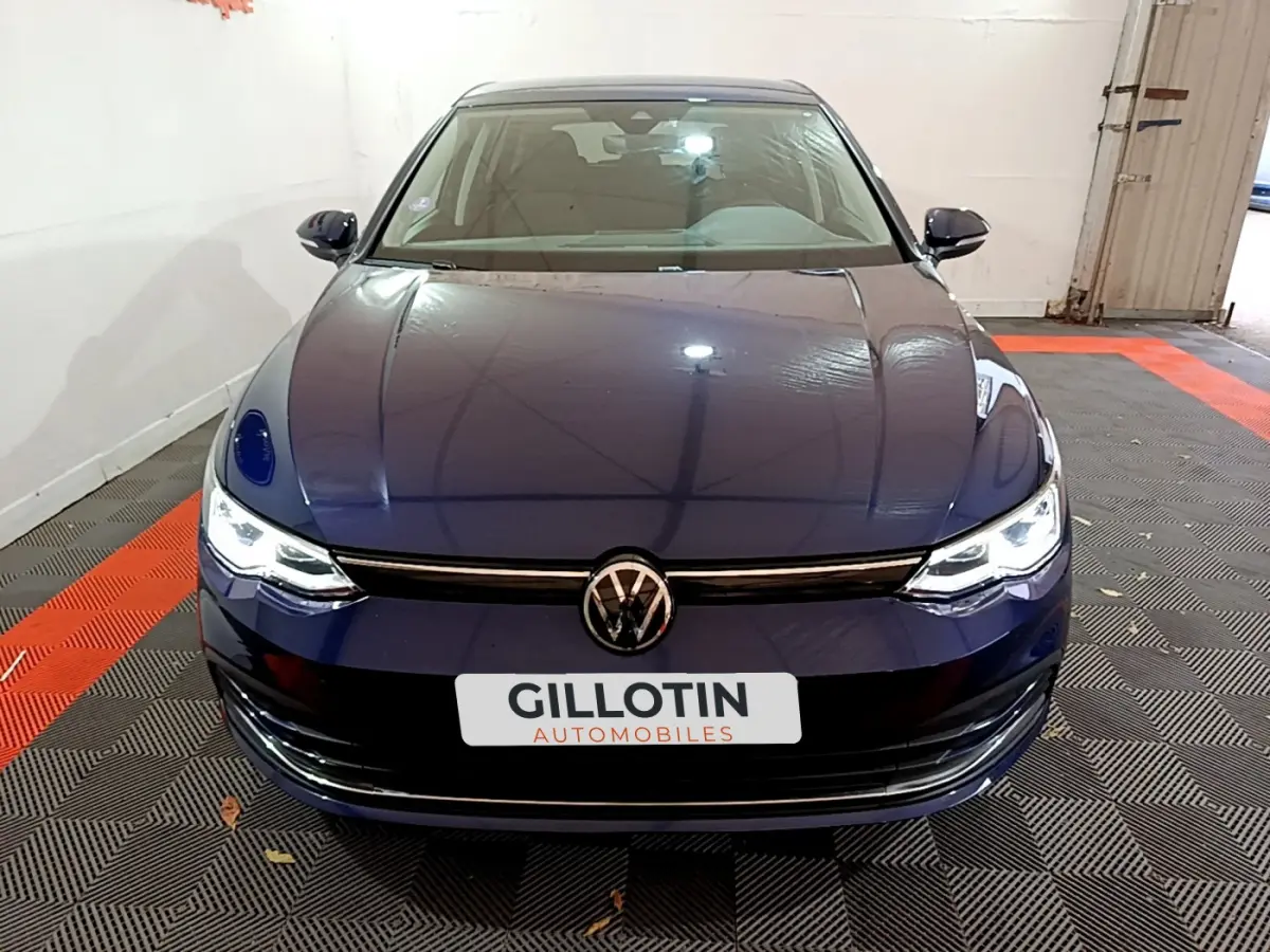 Vue frontale d'une Volkswagen Golf 1.0 TSI bleu foncé avec phares LED allumés dans un garage.