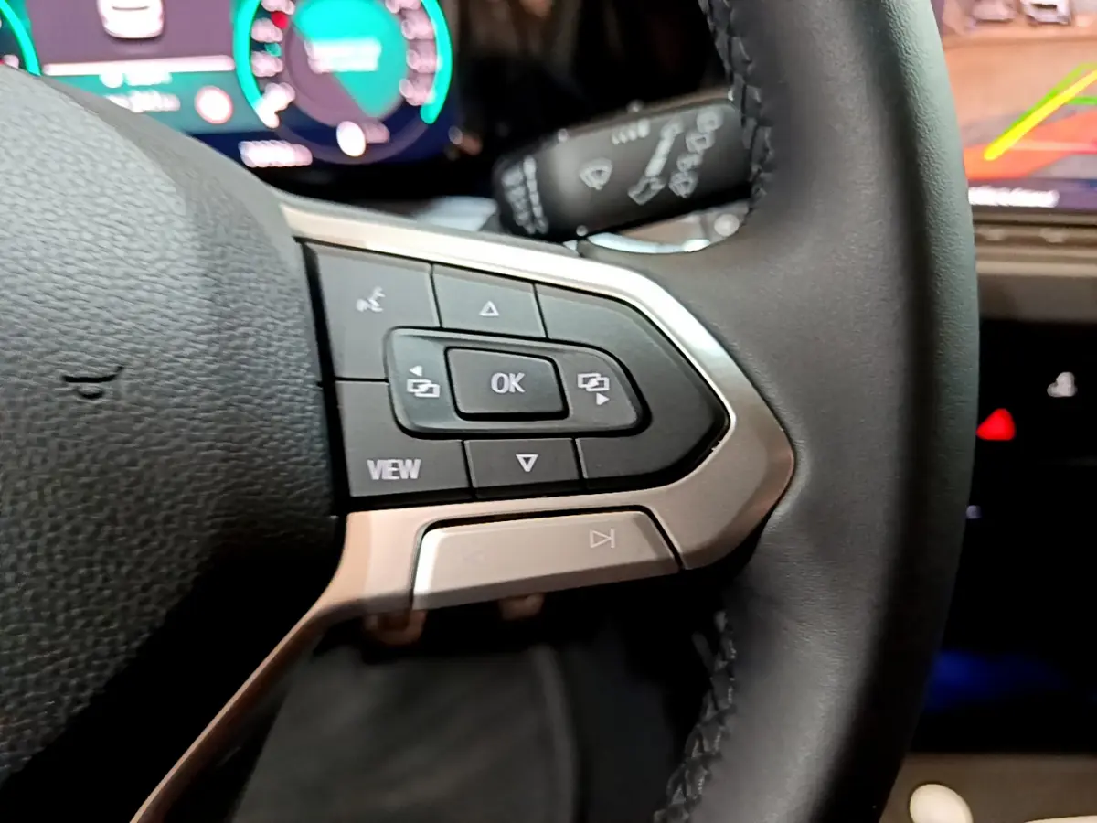 Gros plan sur les commandes gauche du volant cuir noir d'une Volkswagen Golf bleue, avec affichage numérique en arrière-plan.