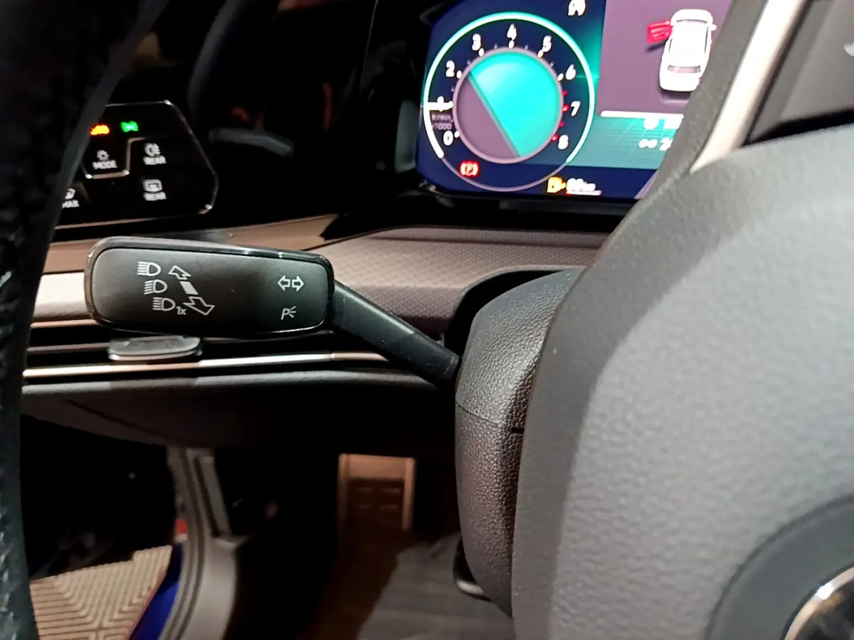 Gros plan sur le commodo gauche du volant d'une Volkswagen Golf 2022, avec tableau de bord numérique coloré en arrière-plan.