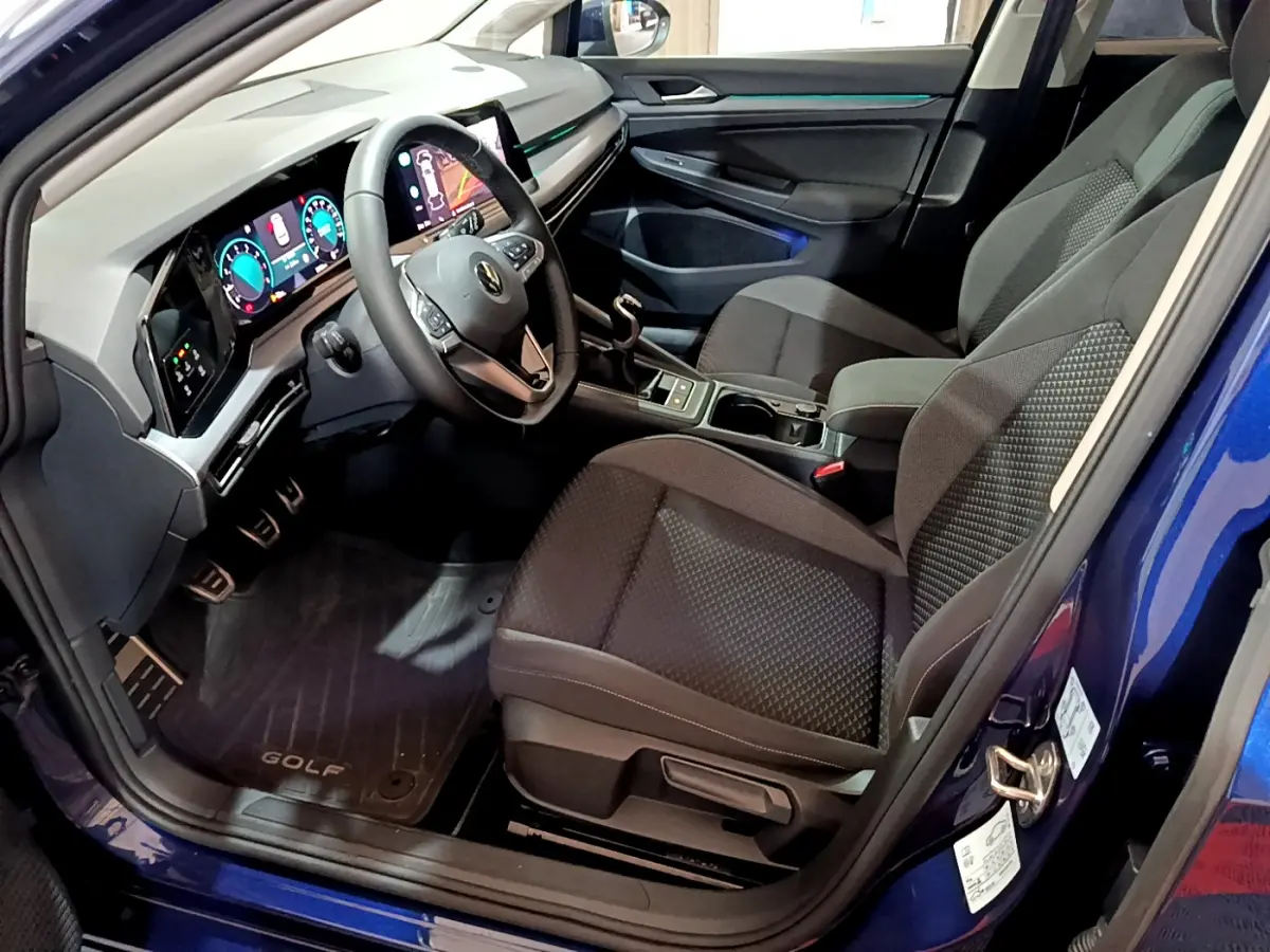 Vue intérieure côté conducteur d'une Volkswagen Golf bleu 2022 avec tableau de bord numérique et sièges noirs tissu.