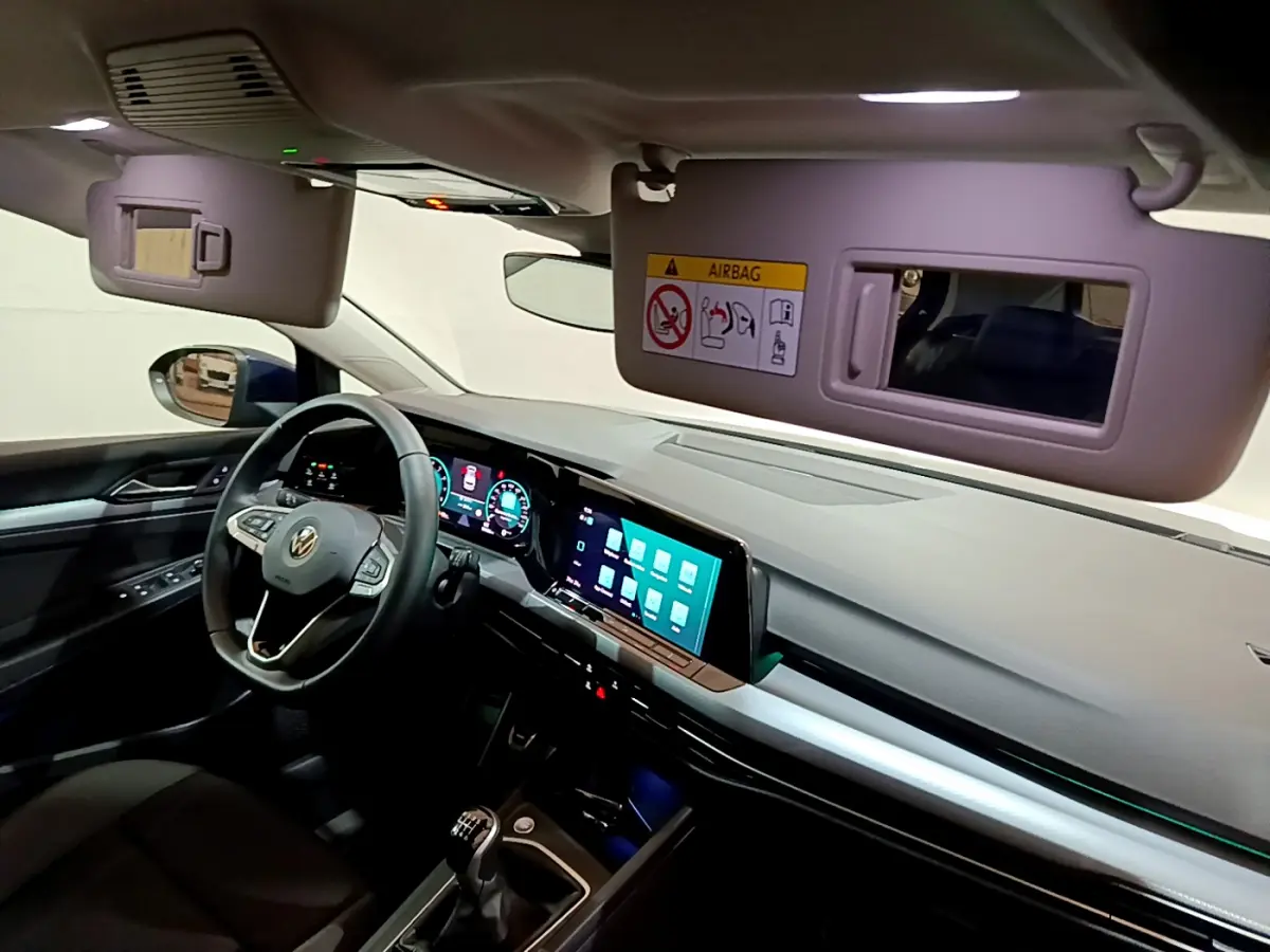 Vue intérieure avant droite de la Volkswagen Golf 1.0 TSI Active 2022, volant cuir, écran tactile et miroir pare-soleil ouvert.