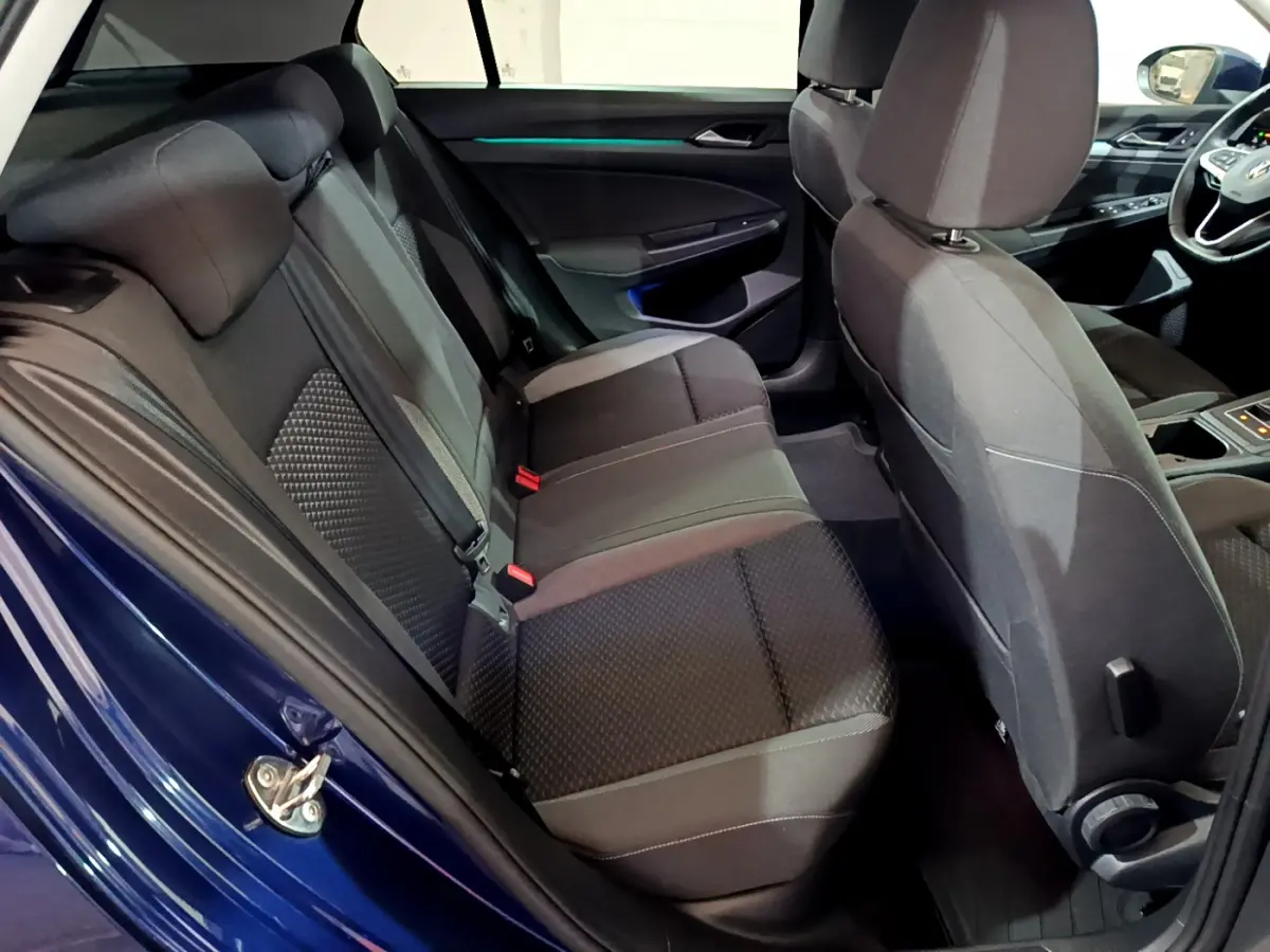 Vue intérieure côté gauche de la banquette arrière noire d'une Volkswagen Golf bleue 2022 avec éclairage d'ambiance bleu.