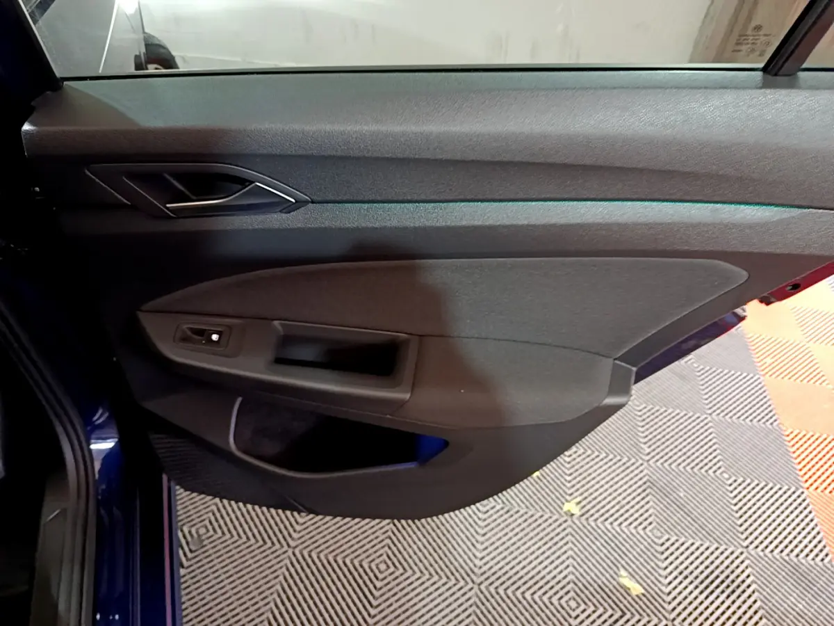 Vue rapprochée de la porte côté gauche de la Volkswagen Golf 1.0 TSI Active 2022 en bleu, avec poignée et commande de vitre.