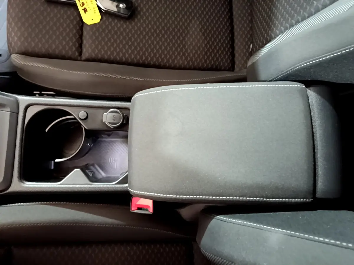 Vue plongeante sur la console centrale noire avec accoudoir et zone de recharge par induction d'une Volkswagen Golf bleue 2022.