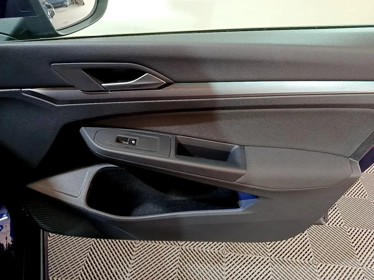 Vue rapprochée de la porte côté gauche d'une Volkswagen Golf bleu 2022, avec poignée et commande de vitre noire.