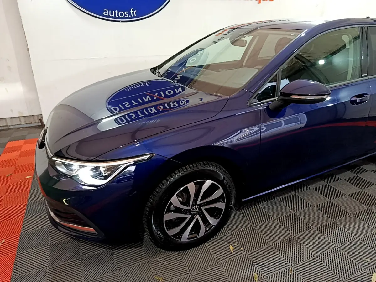 Vue 3/4 avant droit d'une Volkswagen Golf bleu nuit avec phares LED allumés et jantes alliage distinctives.
