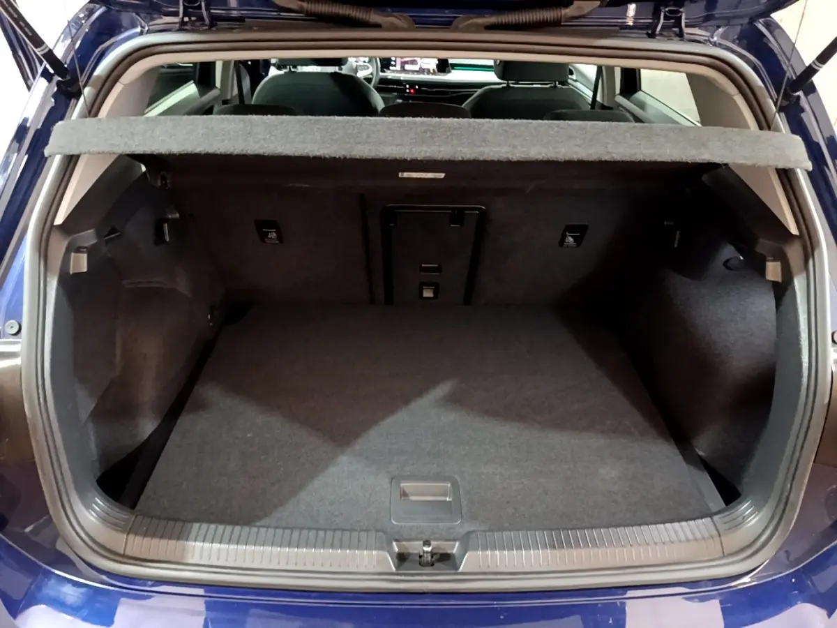 Coffre ouvert vu de l'arrière d'une Volkswagen Golf 1.0 TSI bleu, montrant l'espace de chargement vide et la tablette de séparation.