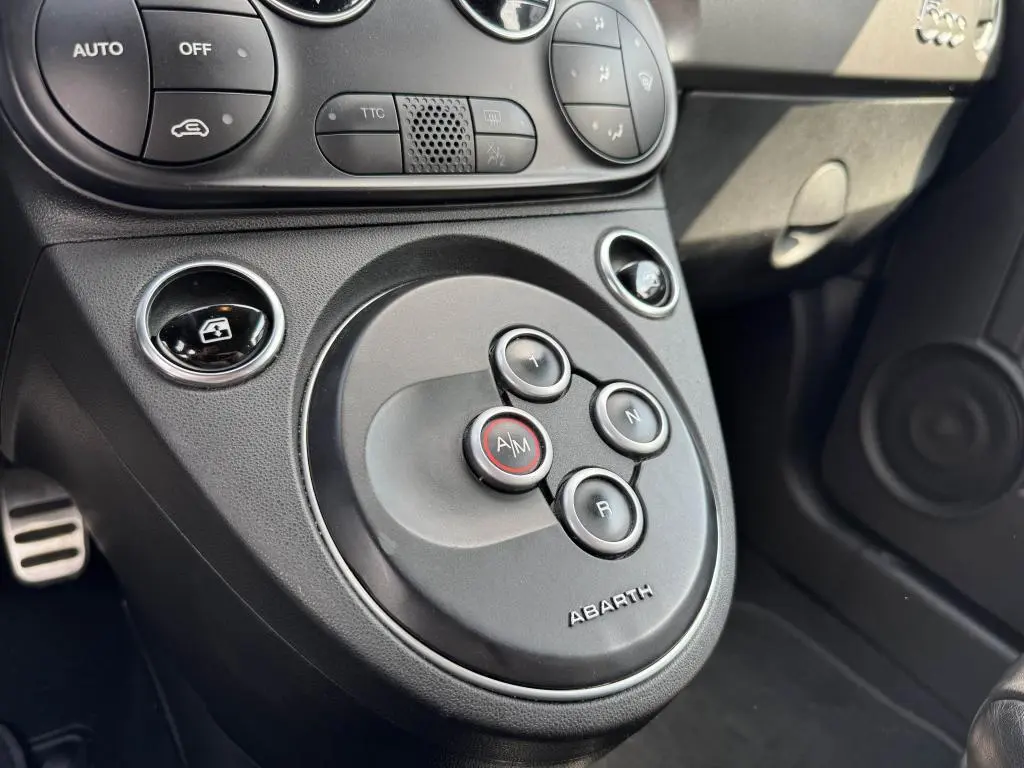 Gros plan sur la console centrale noire de l'Abarth 500 blanc, montrant les boutons de boîte auto avec logo Abarth.