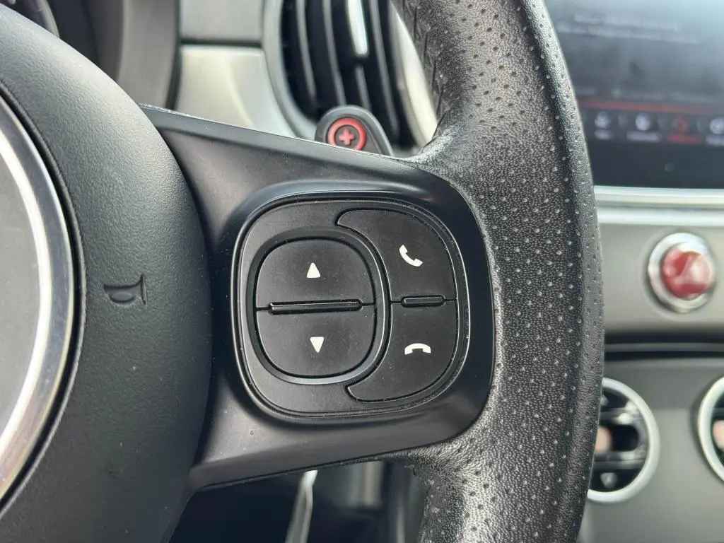 Gros plan sur les commandes noires du volant cuir perforé côté droit de l'Abarth 500 blanc, tableau de bord en arrière-plan.