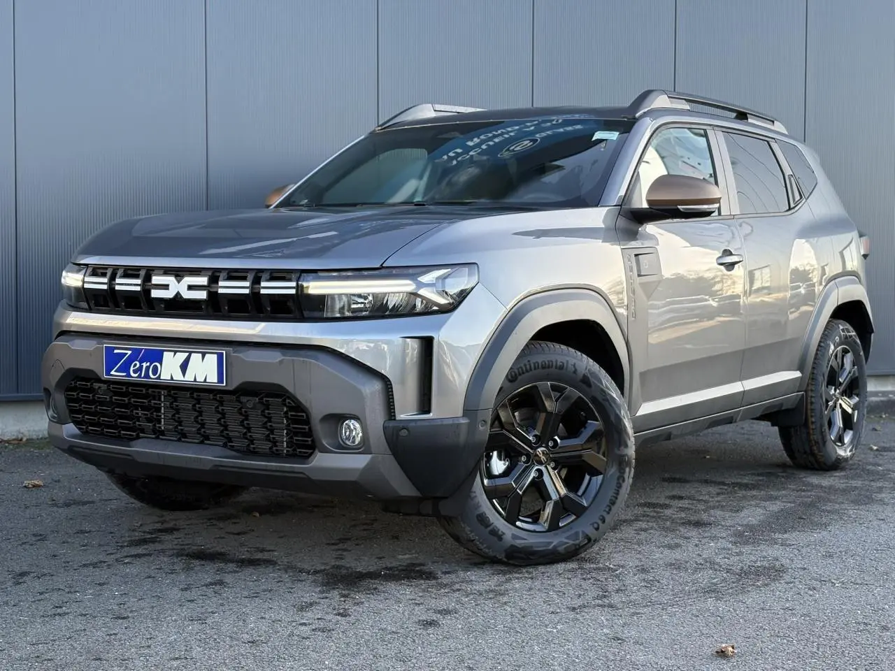 SUV Dacia Duster ECO-G 120 gris schiste en 3/4 avant droit, avec jantes alliage noires et barres de toit.