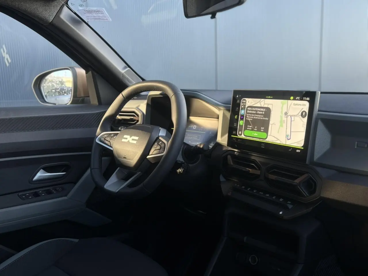 Vue intérieure côté conducteur du Dacia Duster 2026 gris, avec volant multifonction et écran tactile central affichant la navigation.